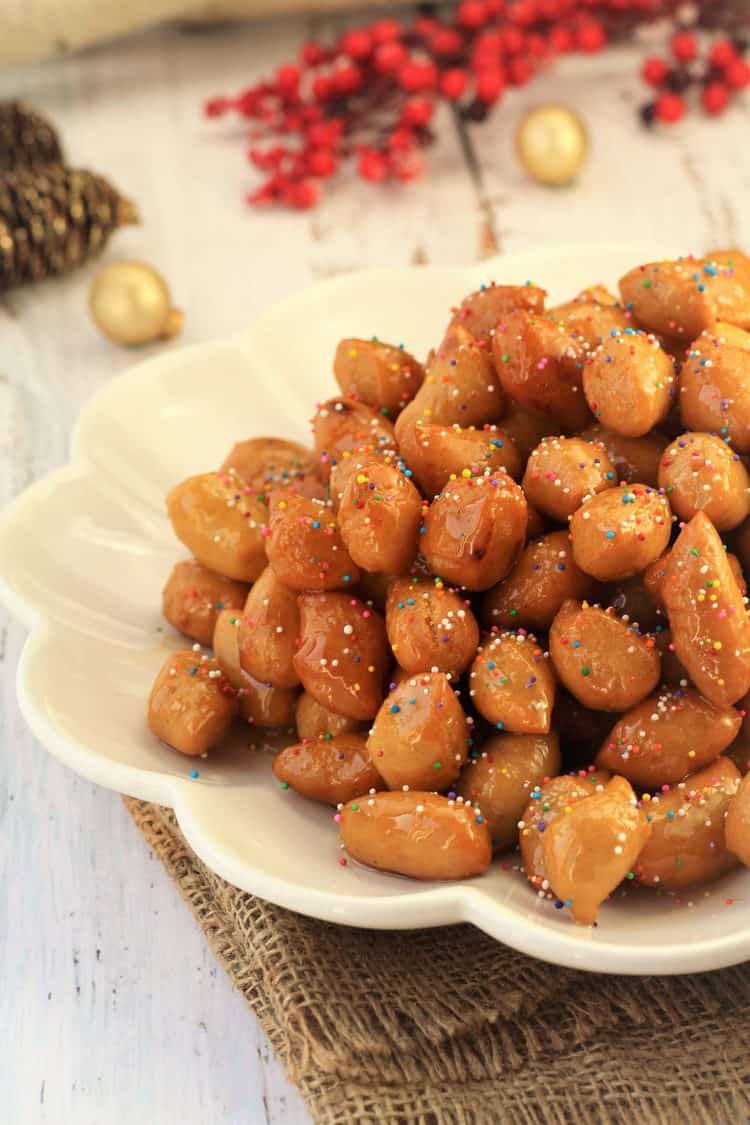 pignolata honey balls piled in a mound on white scallop edged plate 