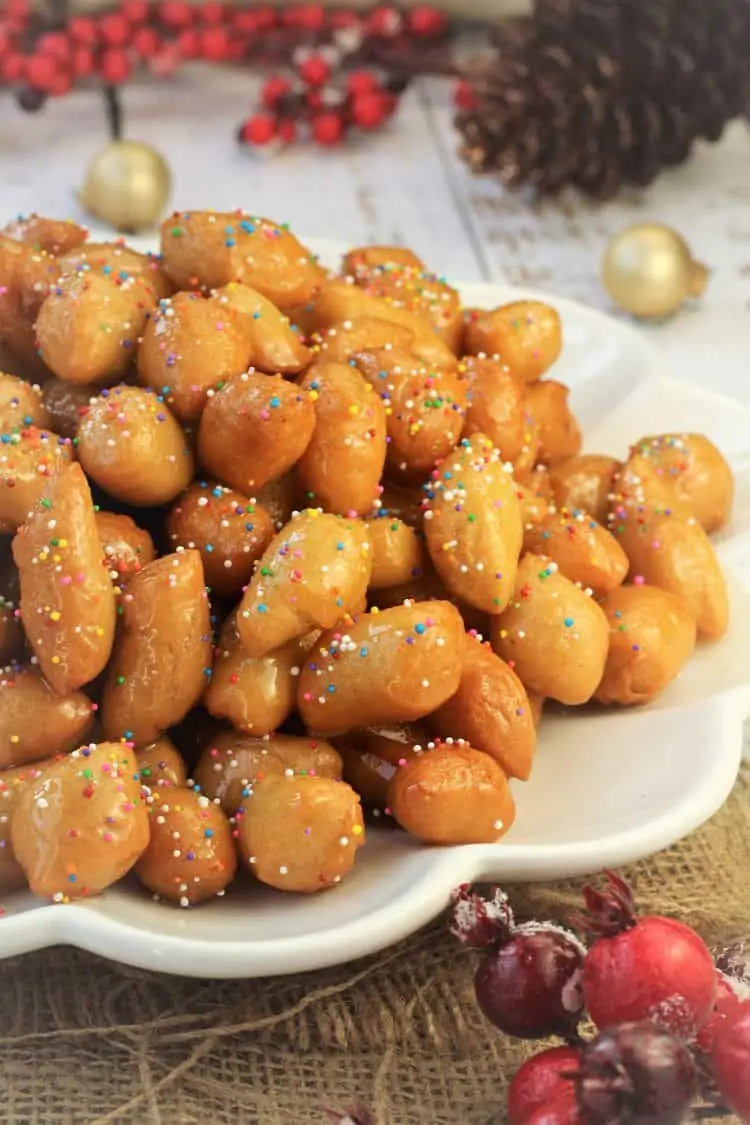 pignolata honey balls in a mound on white plate sprinkled with candy sprinkles