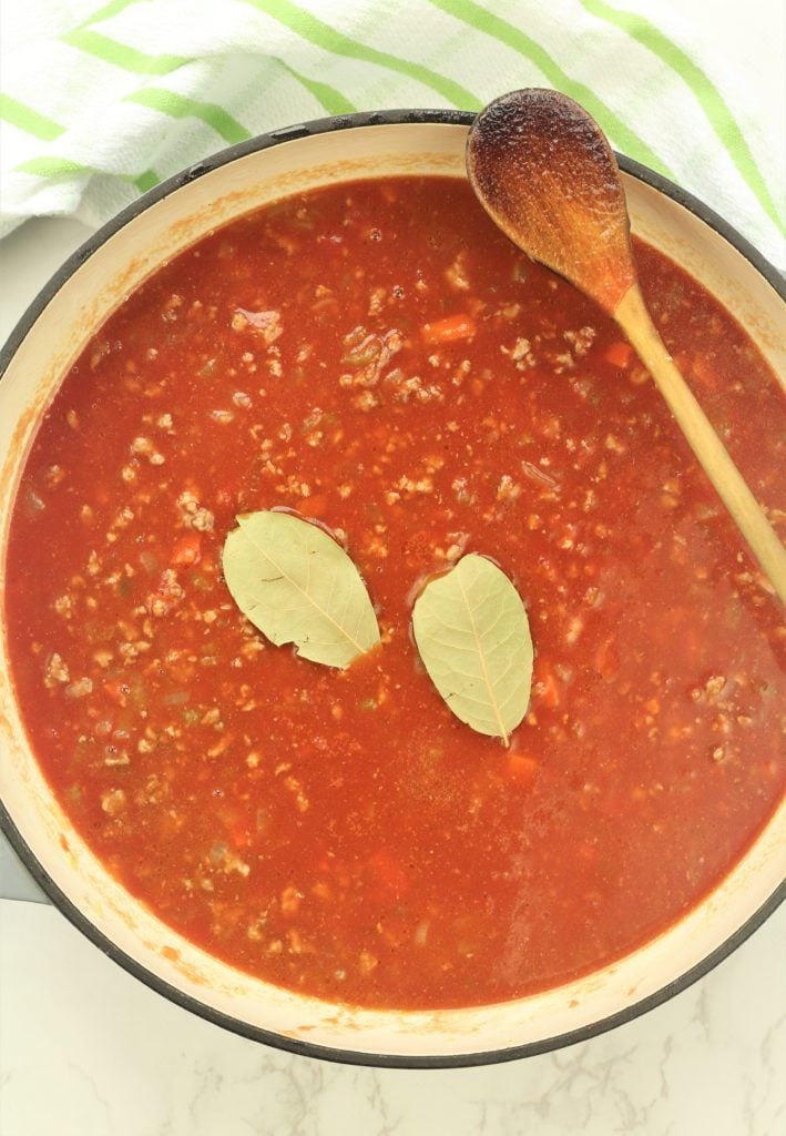 meat sauce with bay leaves in large skillet with wooden spoon
