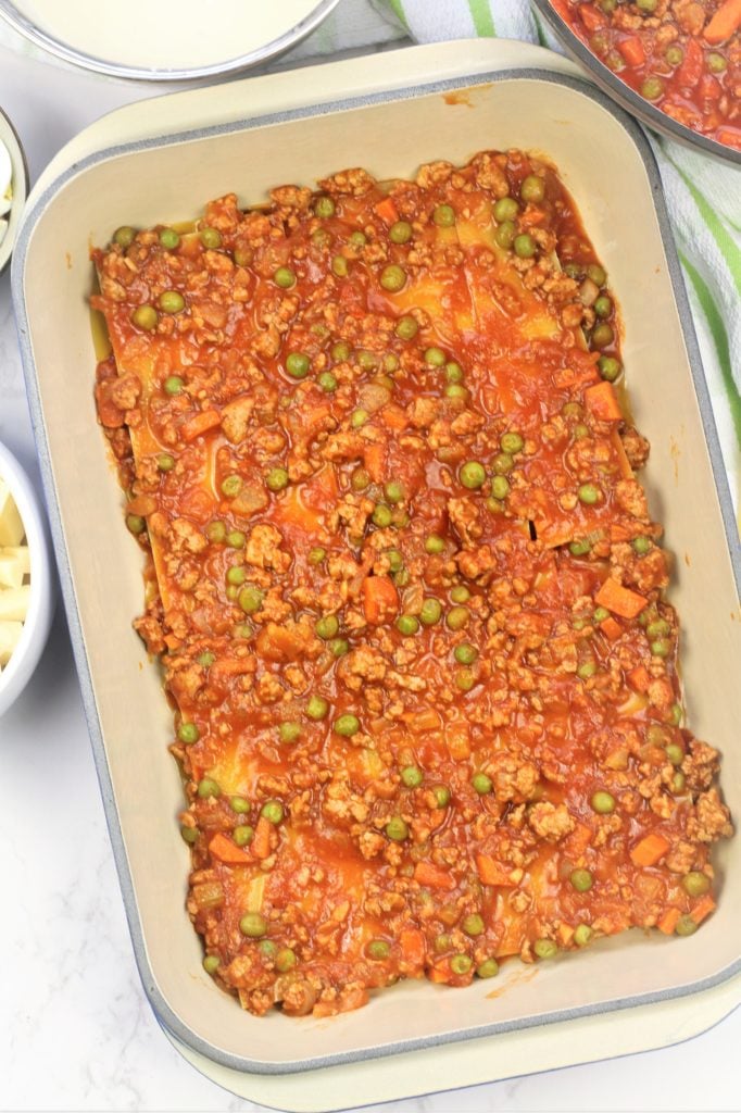 assembling lasagna with ragu with peas