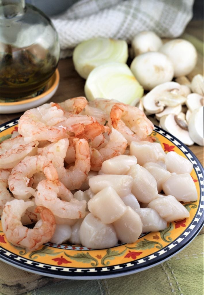 raw shrimp and scallops on plate surrounded by sliced mushrooms and onions