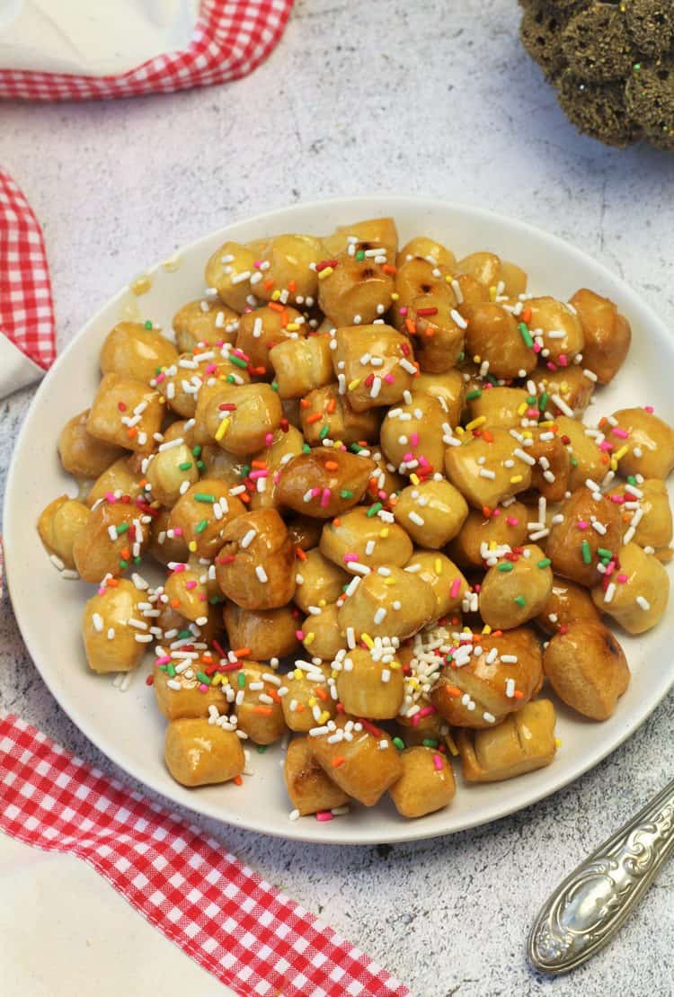 pignolata honey balls with candy sprinkles on white plate
