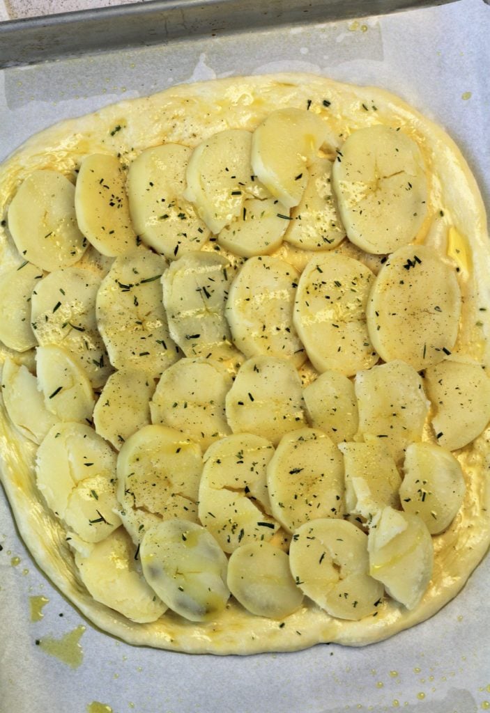 pizza dough topped with overlapping sliced potatoes and rosemary