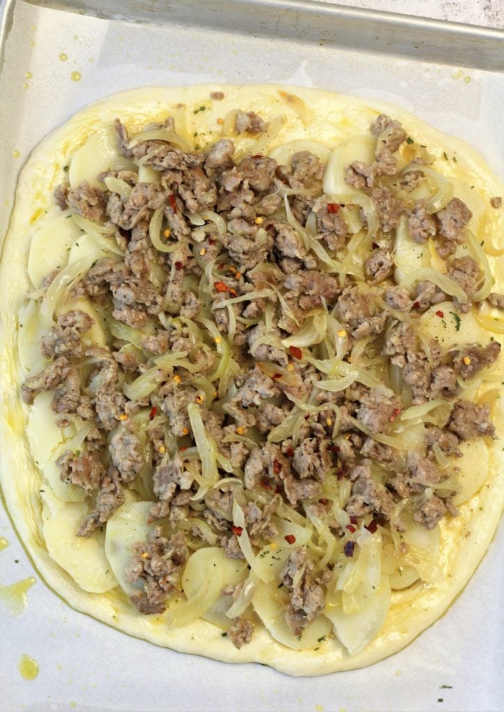 pizza dough topped with sausage meat and sliced potatoes