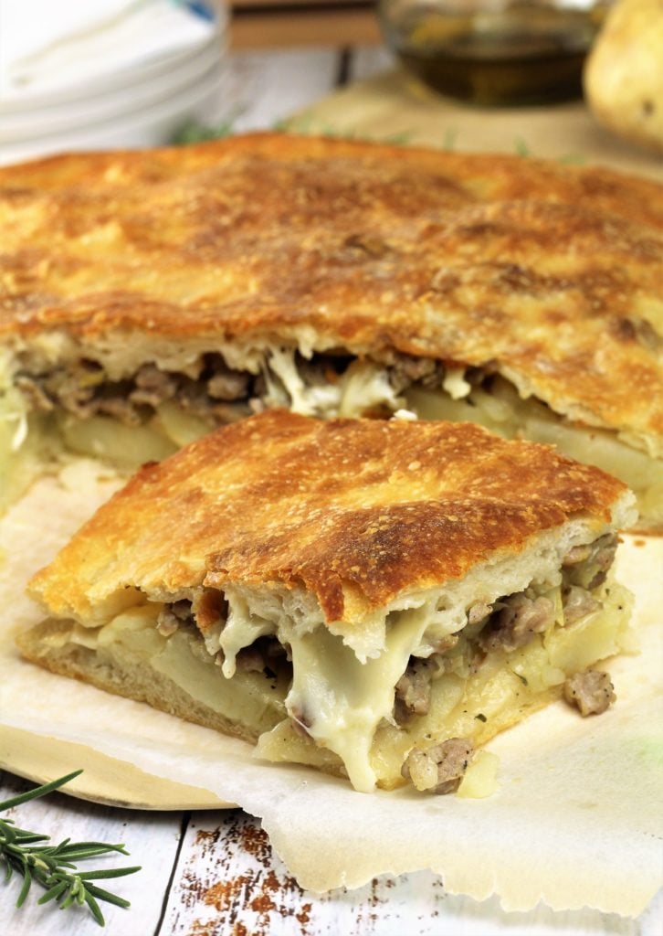 wedge of scacciata filled with potatoes and sausage on wood board 