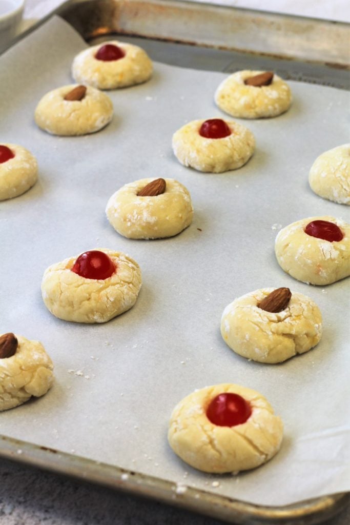 orange juice cookies topped with maraschino cherries or almonds on baking sheet