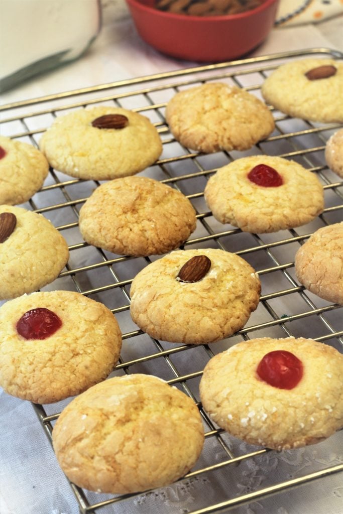 orange juice cookies topped with almonds and maraschino cherries on wire rack