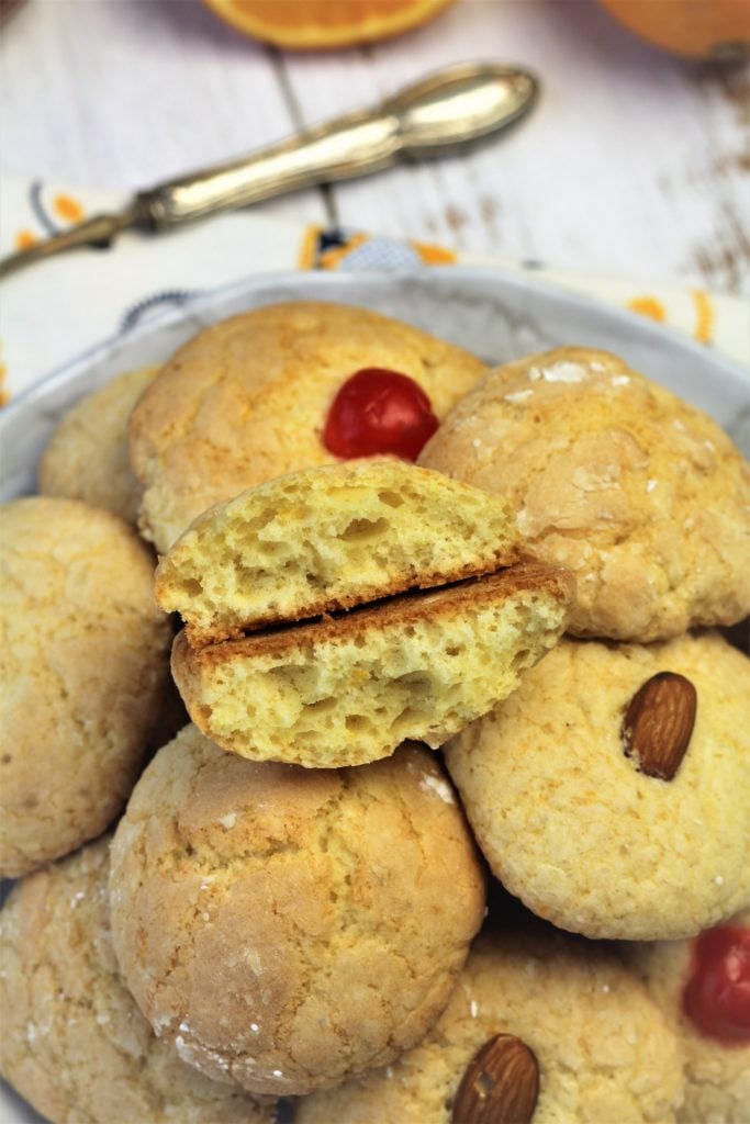 orange juice cookies piled on white plate with one cut open to reveal crumb