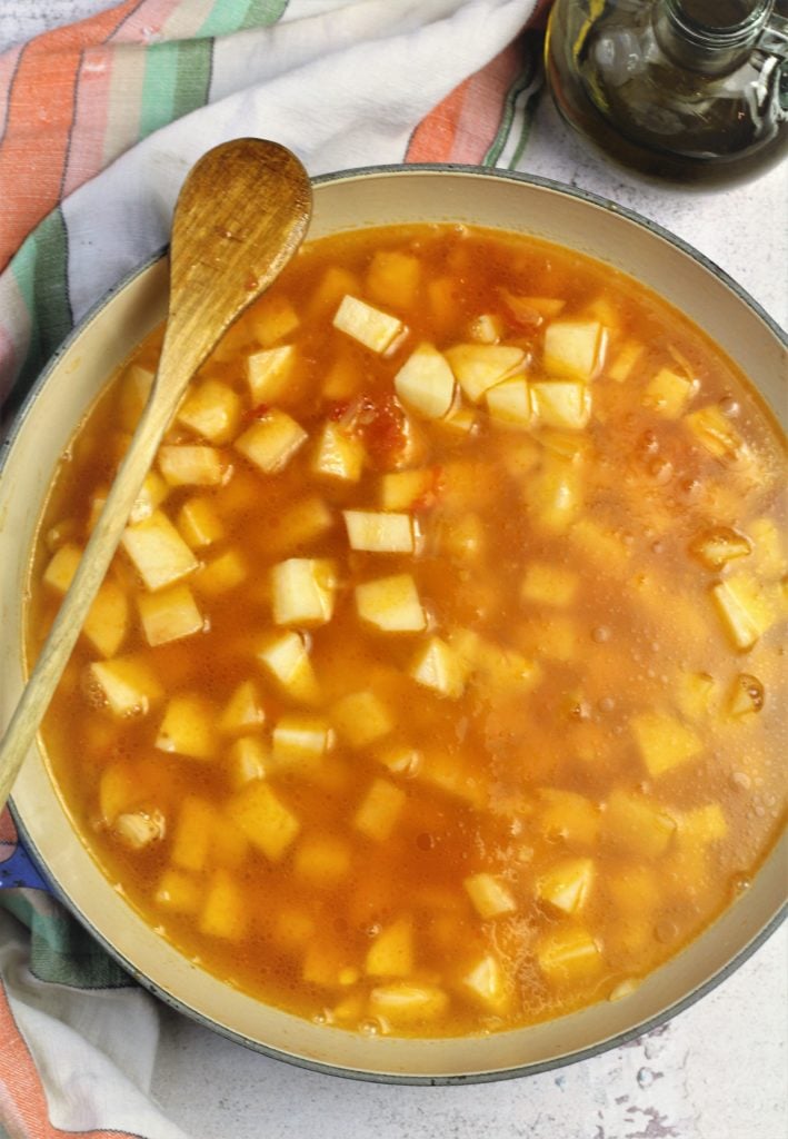 large skillet with cubed potatoes, tomato and diced onion covered with water