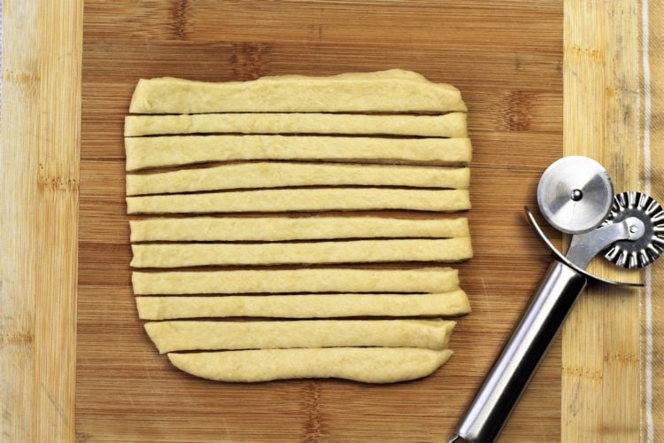 square of rolled dough cut into strips with pasta wheel