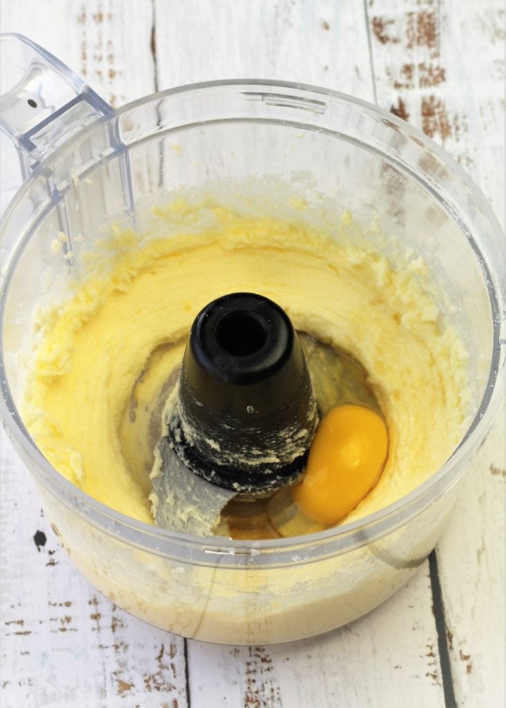 egg added to food processor bowl with creamed butter and sugar