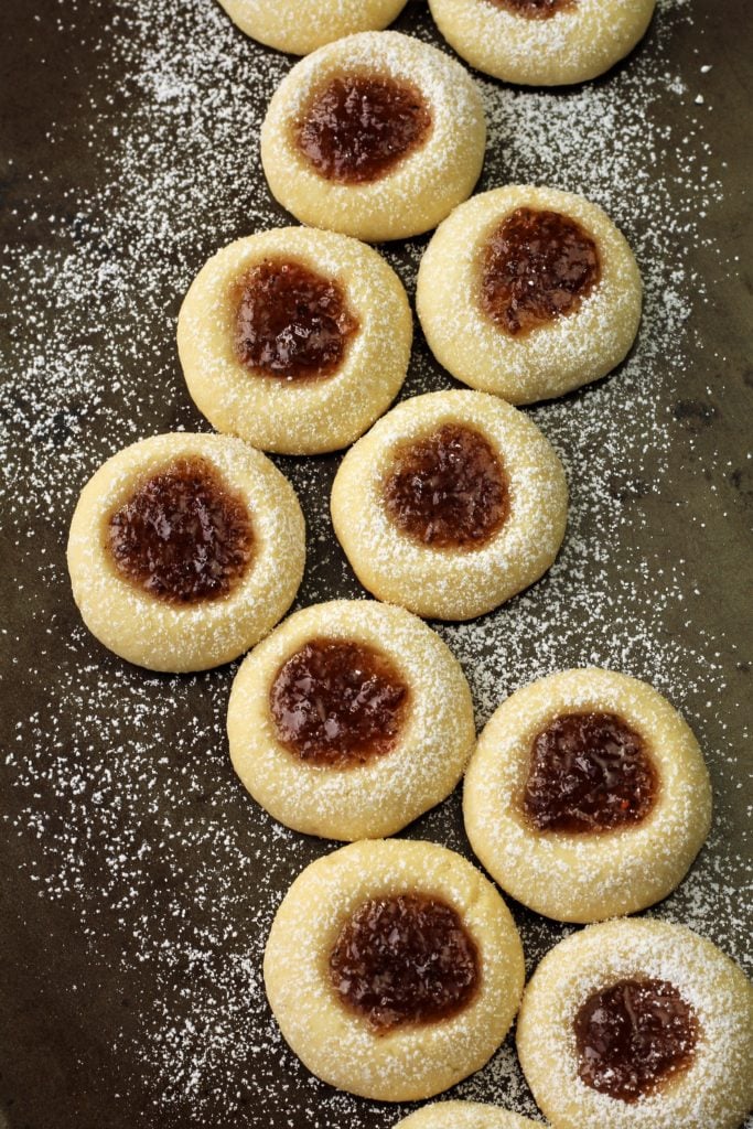 raspberry jam thumbprint cookies dusted with powdered sugar on black background