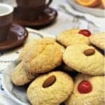 orange juice cookies with maraschino cherries or almonds on top piled on plate