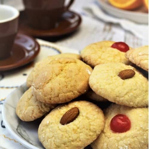 orange juice cookies with maraschino cherries or almonds on top piled on plate