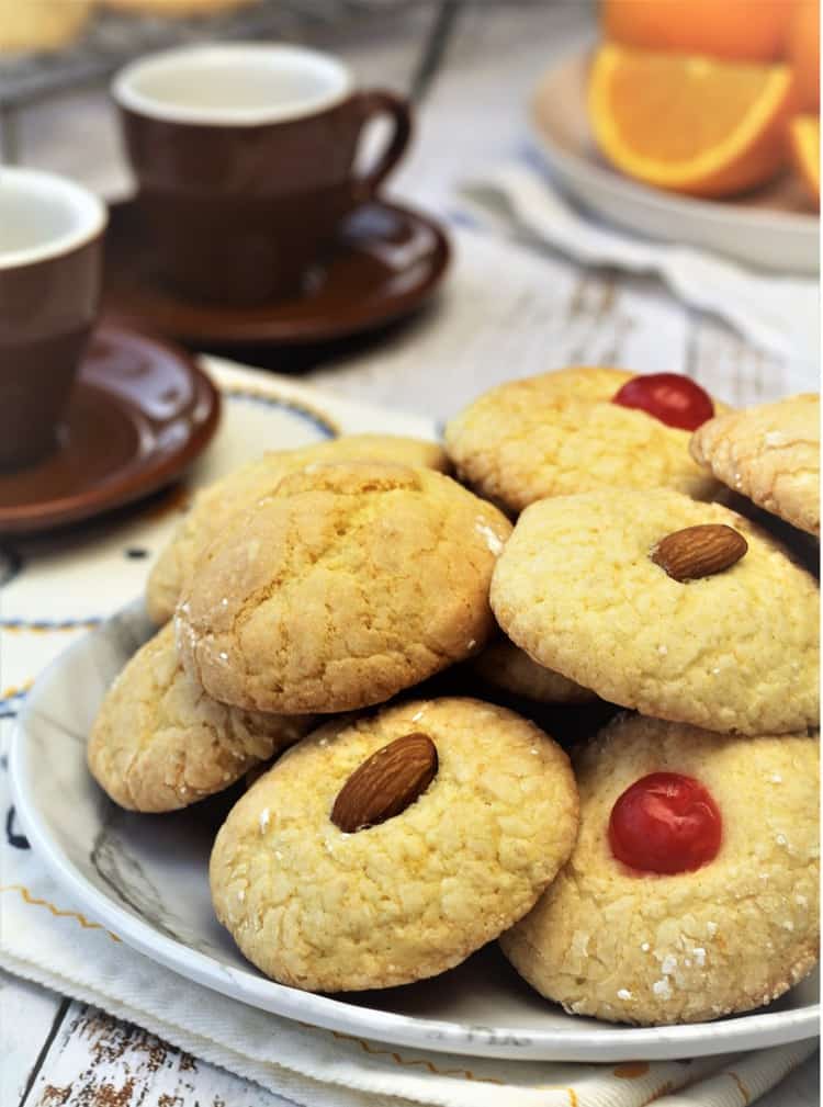 orange juice cookies with maraschino cherries or almonds on top piled on plate