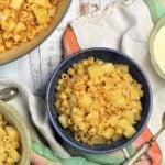 bowl of pasta with potatoes surrounded by pot, spoon and cheese bowl
