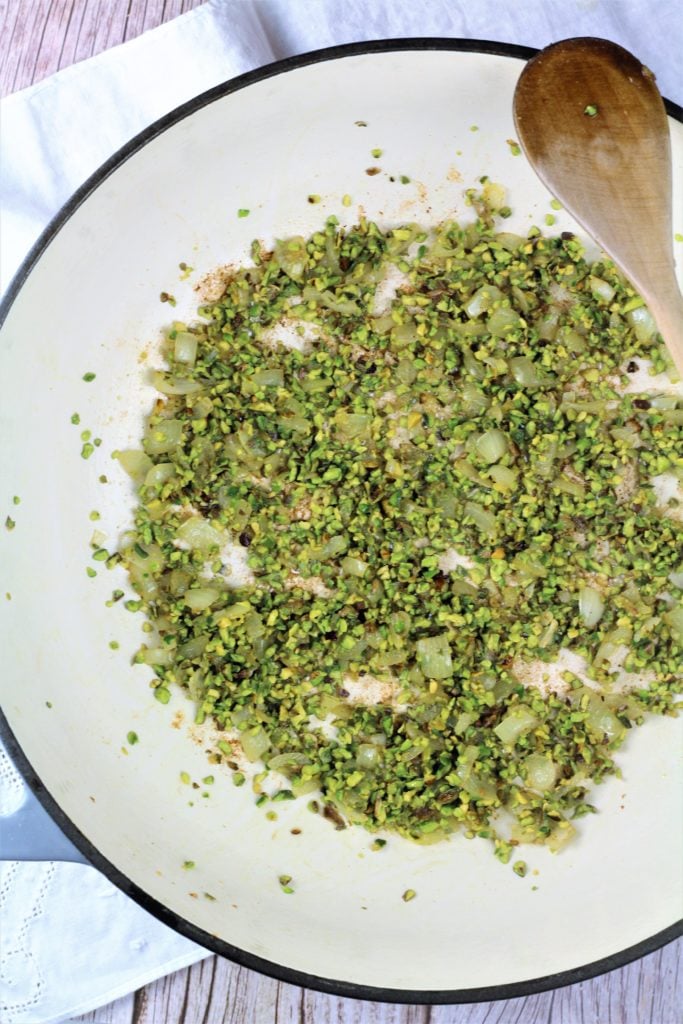 large skillet filled with sautéed onion and crushed pistachios