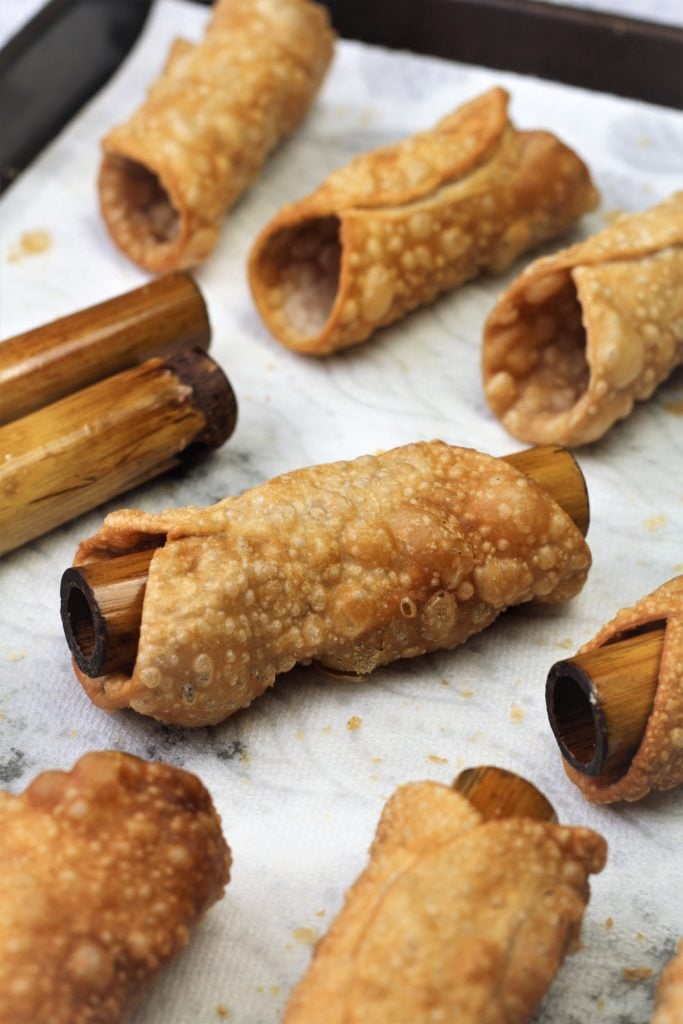 fried cannoli shells with bamboo dowels on paper towel covered tray