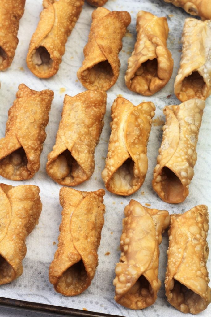 fried cannoli shells resting on paper towel covered tray