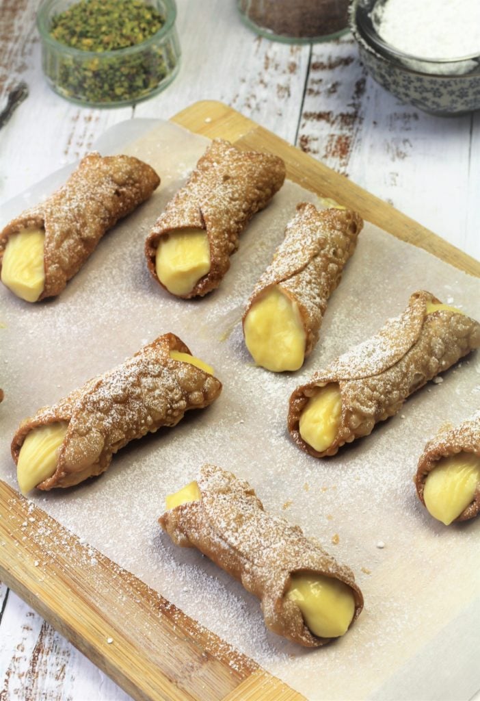 cannoli filled with pastry cream and dusted with powdered sugar on parchment covered wood board