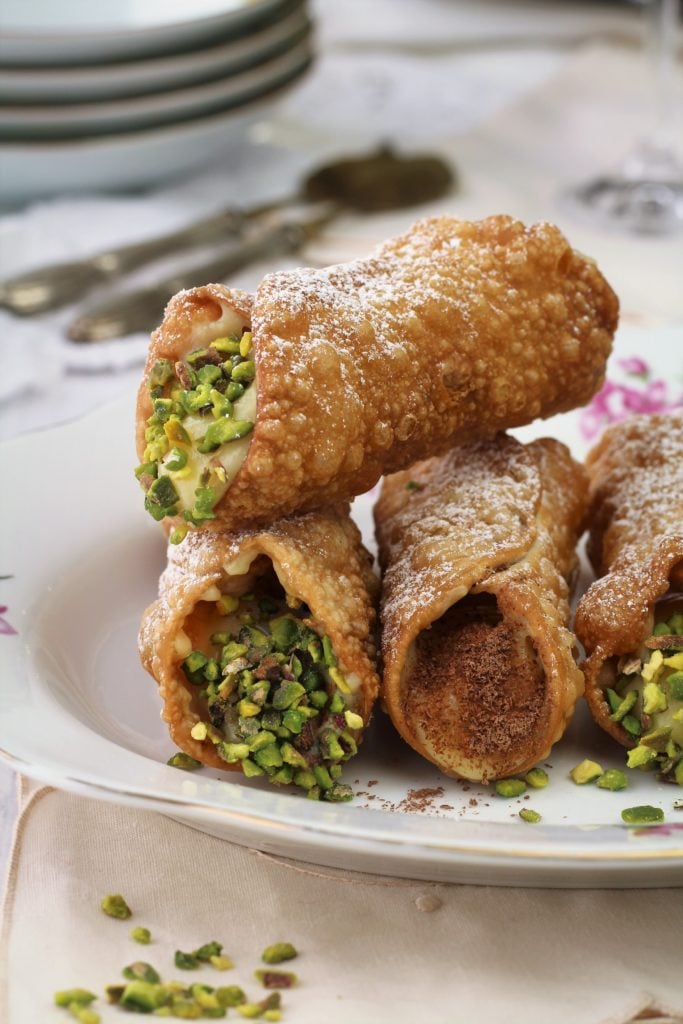 cannoli with pastry cream topped with pistachios piled on plate