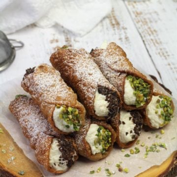 cannoli filled with ricotta cream piled on wood board