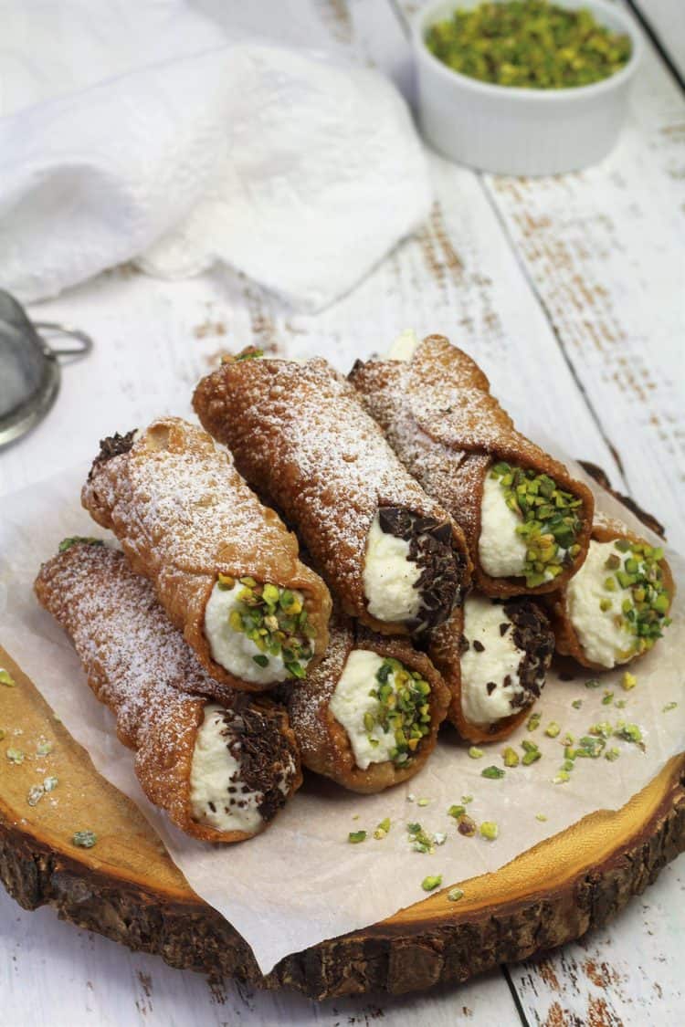 cannoli filled with ricotta cream piled on wood board