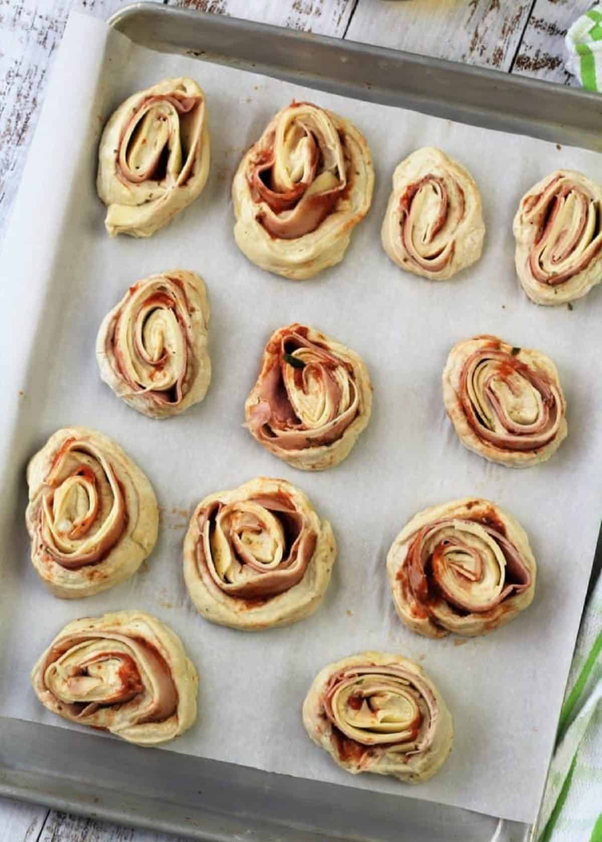 Pizza rolls dough filled with prosciutto cotto and provolone cheese placed on baking sheet.