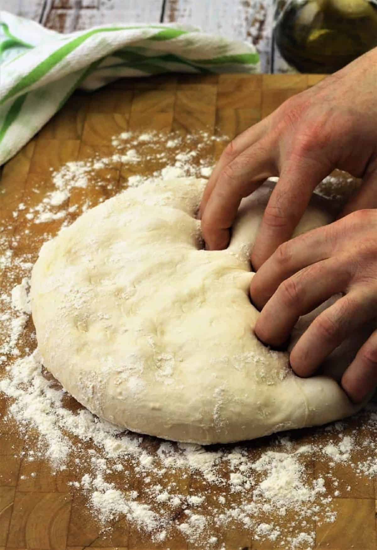 No knead pizza dough on wood board pressed down with fingertips.