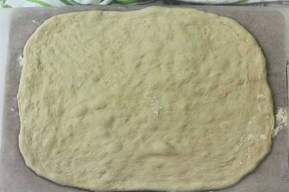 Flattened no knead pizza dough in rectangular shape for pizza rolls.