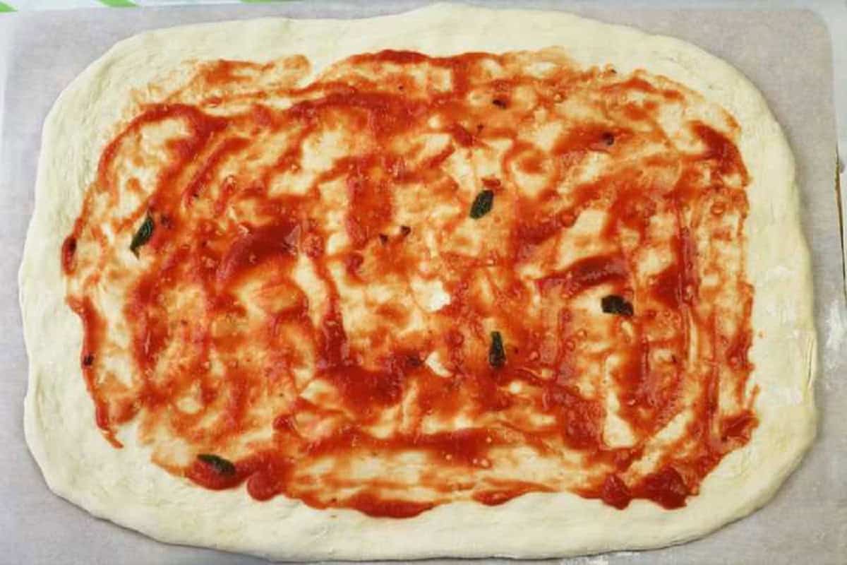 Tomato sauce topped flattened pizza dough for pizza rolls.