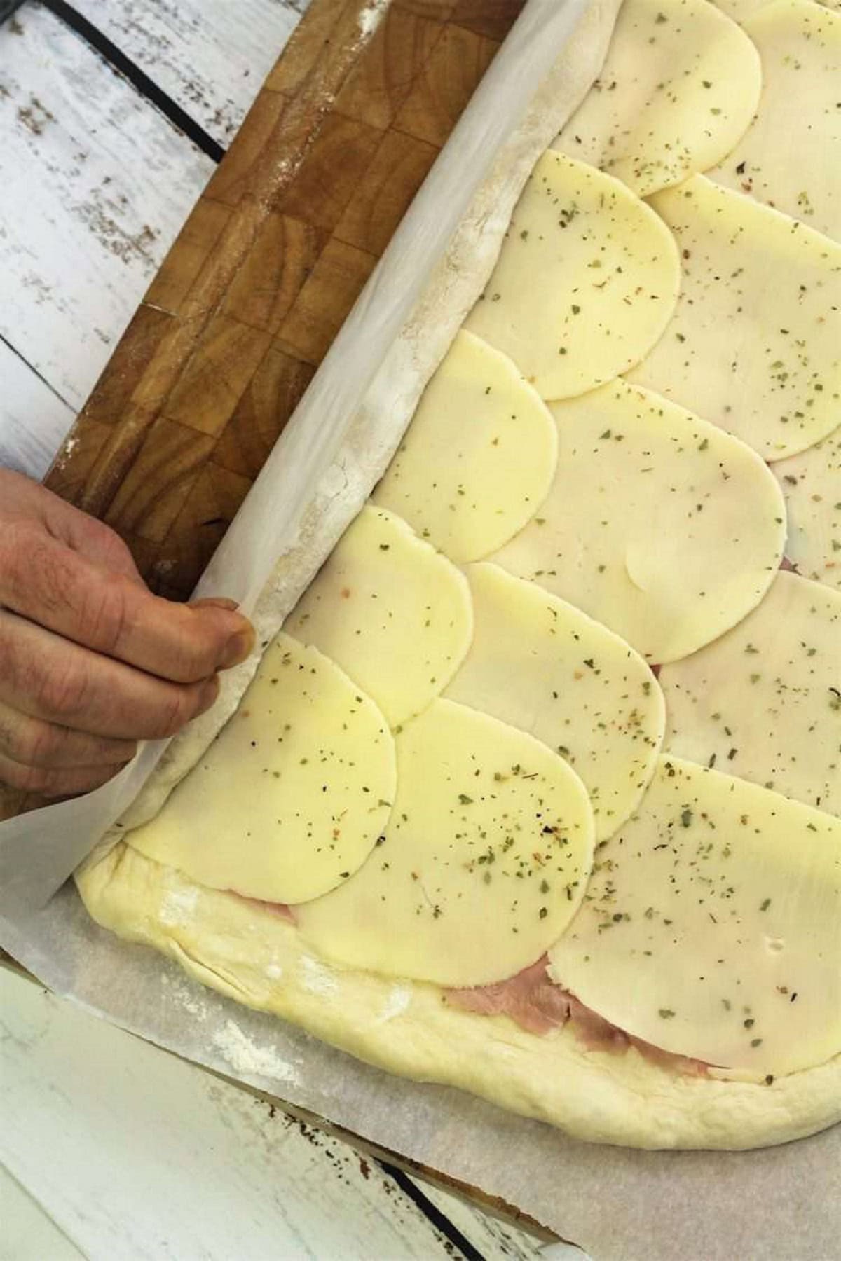 Rolling pizza dough topped with provolone cheese for pizza rolls.