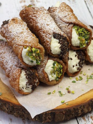 ricotta filled cannoli with chopped pistachio piled on wood board