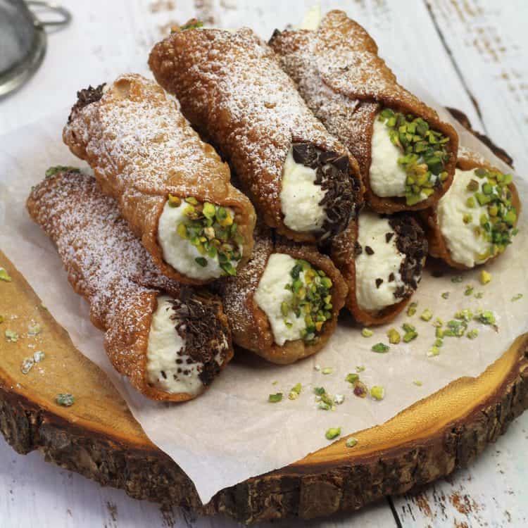 ricotta filled cannoli with chopped pistachio piled on wood board