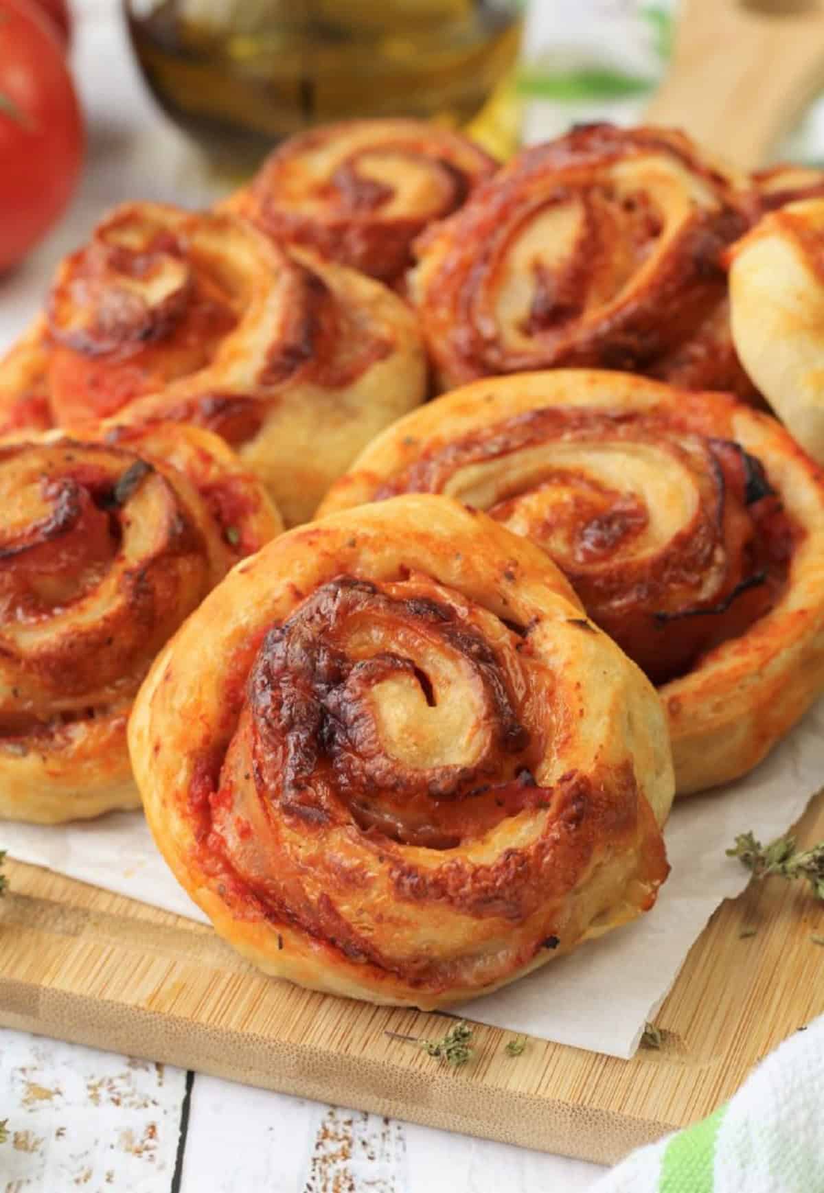 Homemade pizza rolls with ham and cheese piled on wood board.