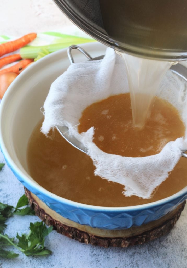 straining broth in a sieve covered with cheese cloth over a bowl 
