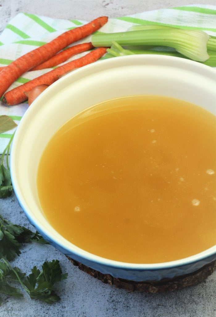 large bowl filled with chicken broth and carrots and celery sticks behind it