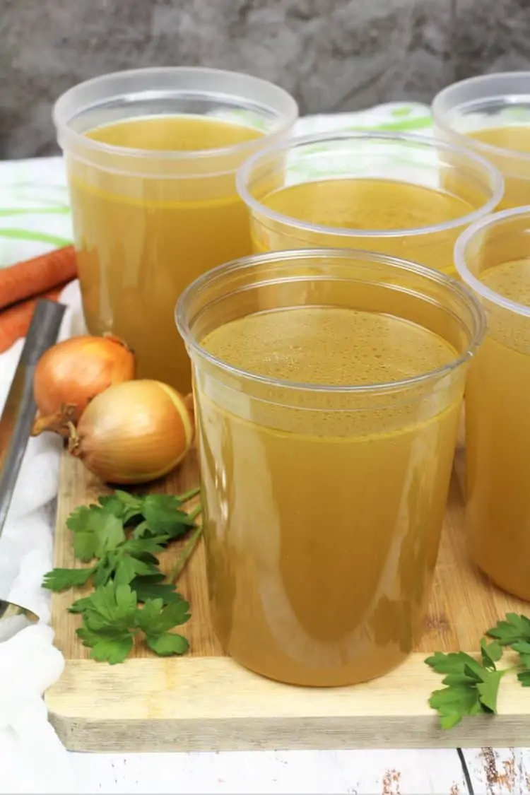 one liter plastic containers filled with homemade chicken broth on wood board with parsley sprigs