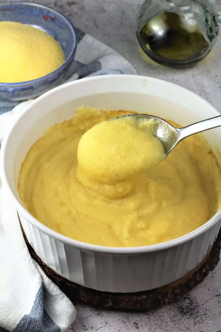 white casserole dish with creamy polenta served with a spoon