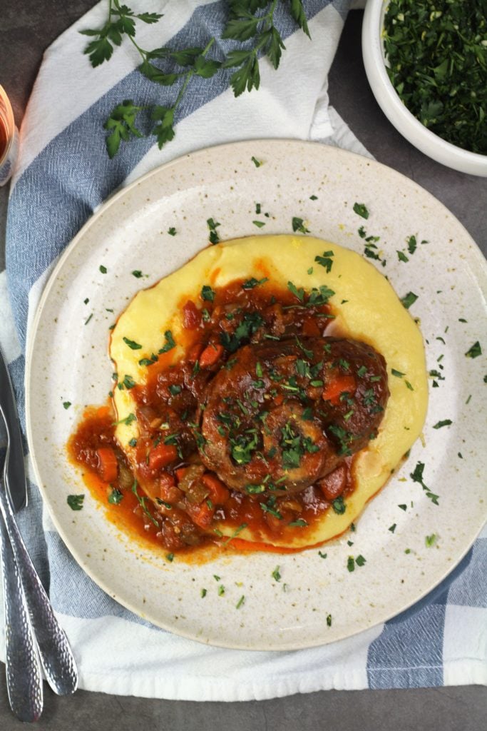 veal osso buco with sauce over polenta on round plate