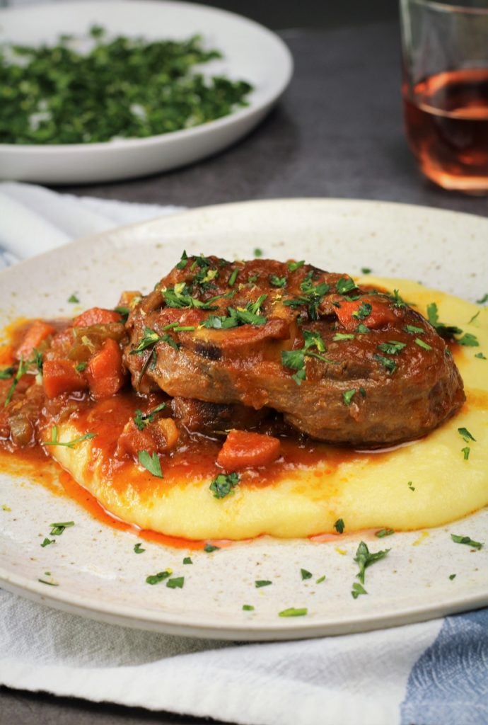 veal osso buco with tomato sauce served over polenta and sprinkled with gremolata