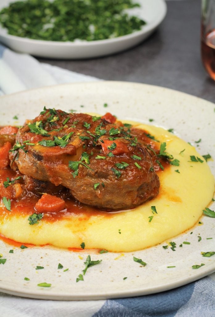 veal osso buco with tomato sauce over polenta topped with parsley gremolata