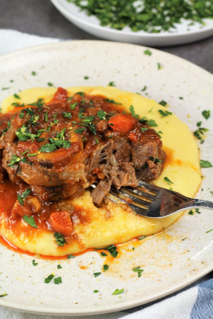 veal osso buco with tomato sauce over polenta with forkful of meat