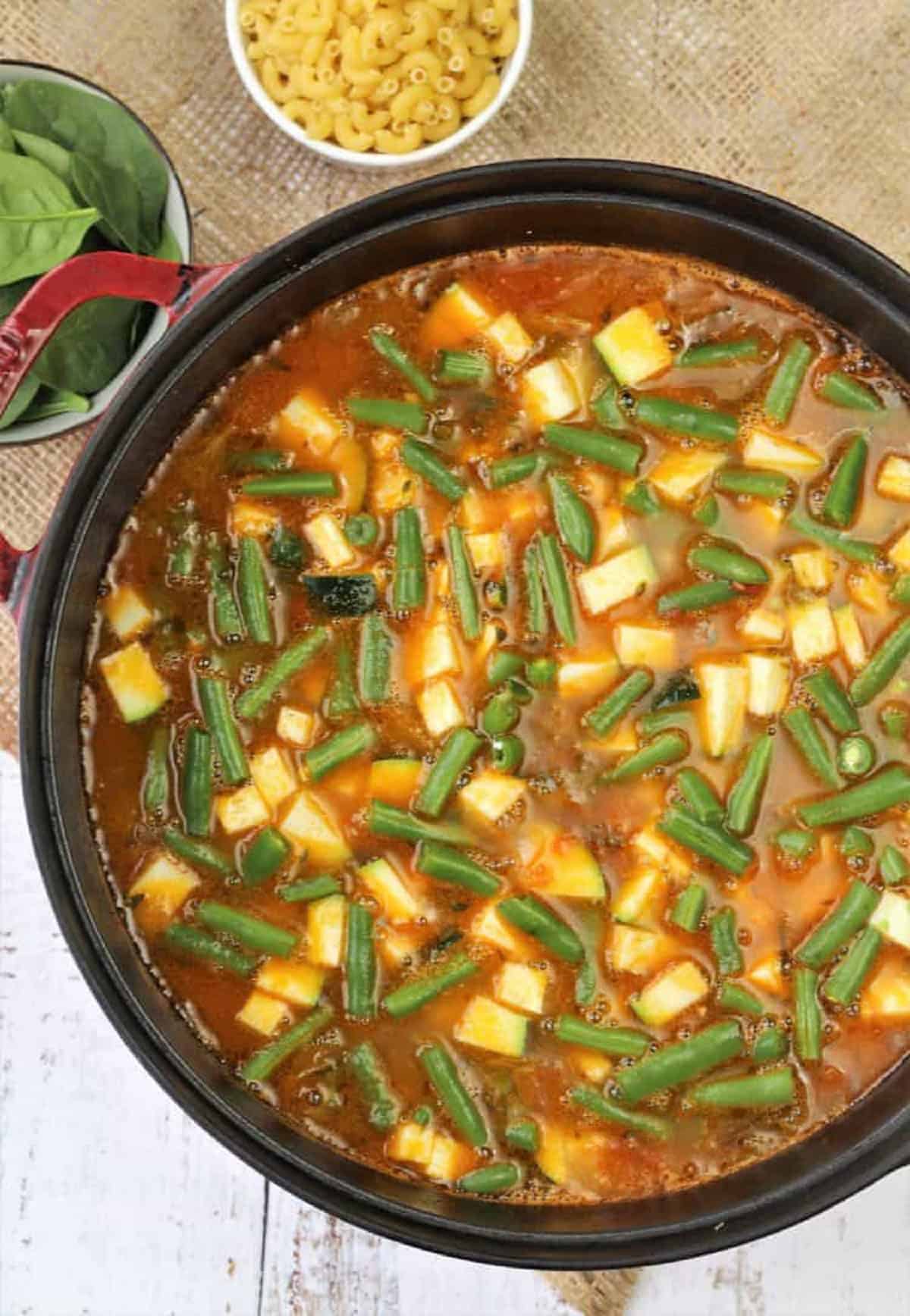 Green beans added to sauce pan with vegetables for minestrone soup.