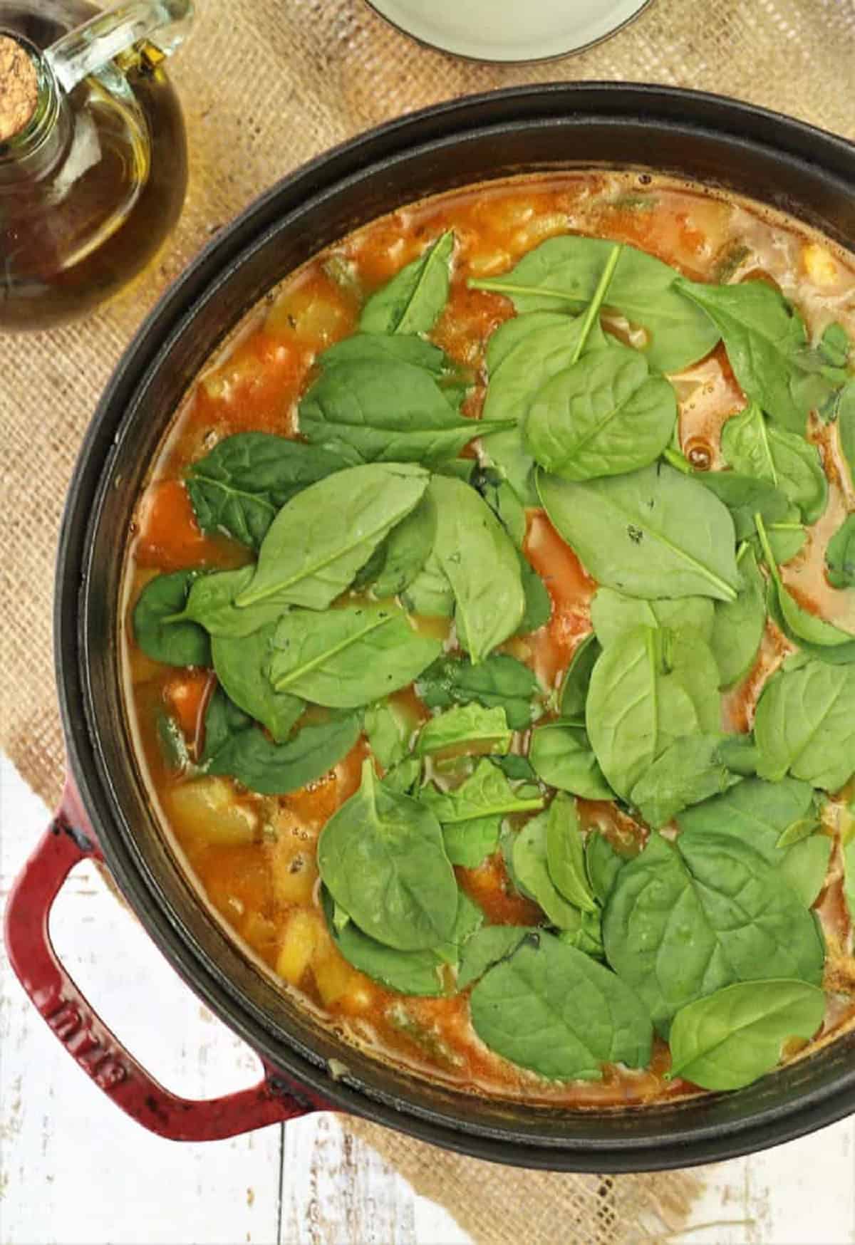 Spinach stirred into sauce pan with minestrone soup.
