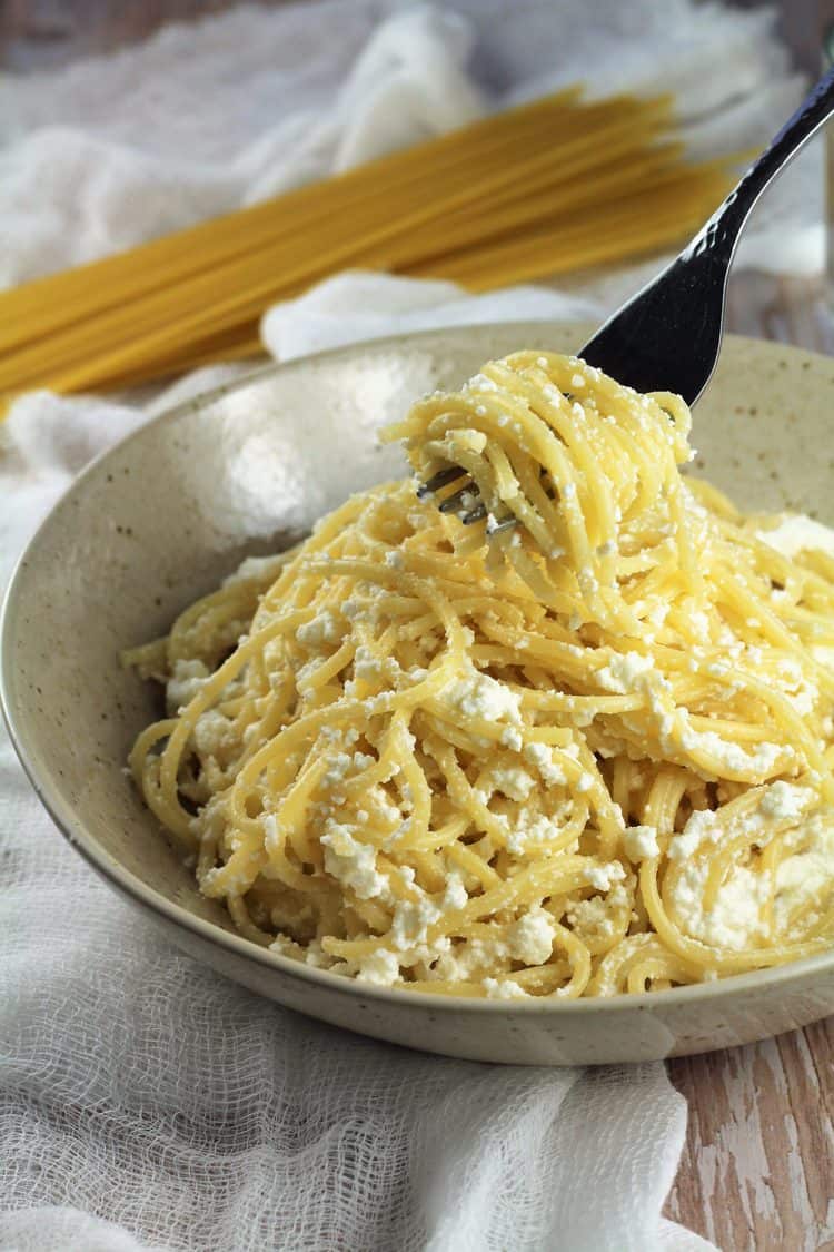 Forkful of spaghetti with creamy sauce over bowl of pastas.
