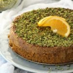 Pistachio orange polenta cake with orange wedge on top.