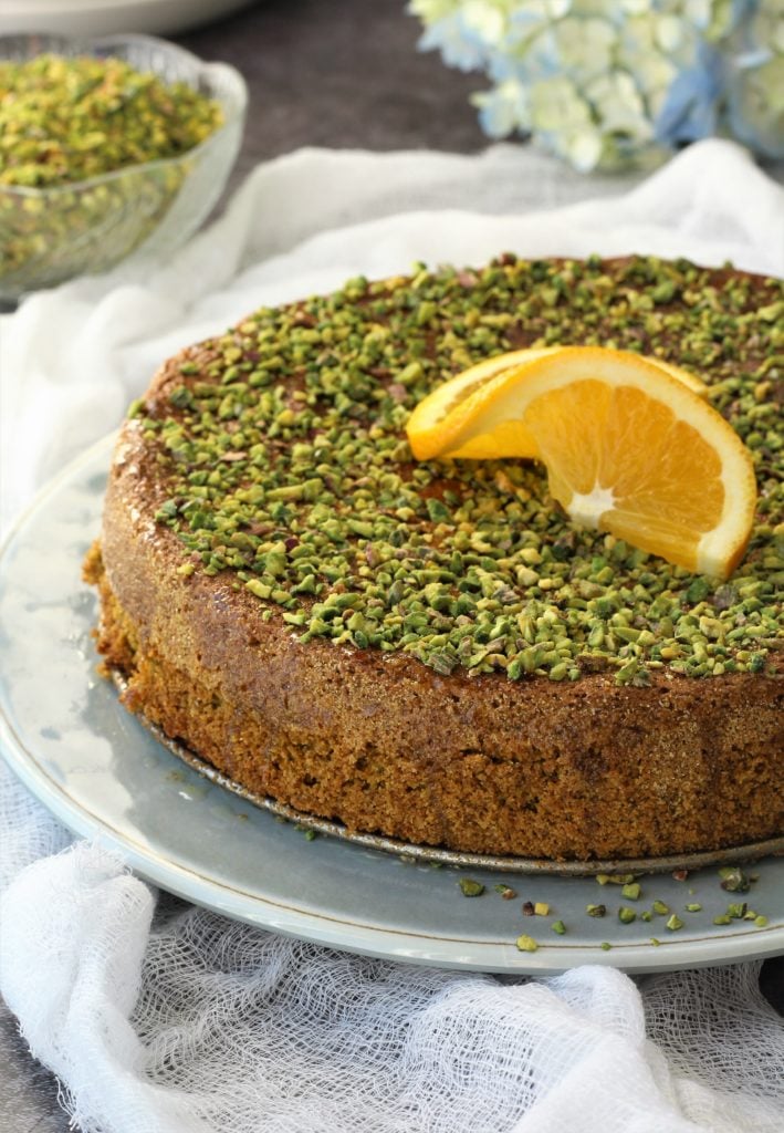 Pistachio orange polenta cake with orange wedge on top.