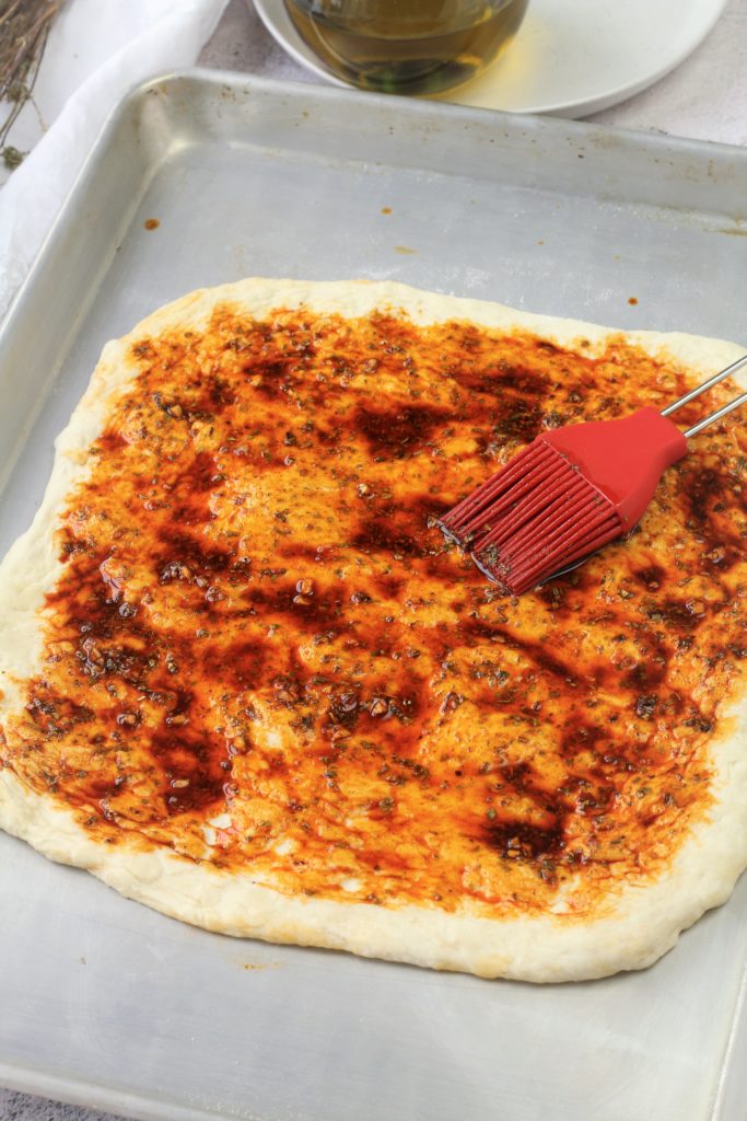 Rectangular pizza dough brushed with paprika, garlic oil mixture.