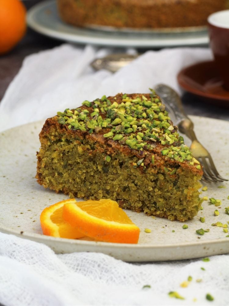 Orange polenta pistachio cake on plate with orange wedges.